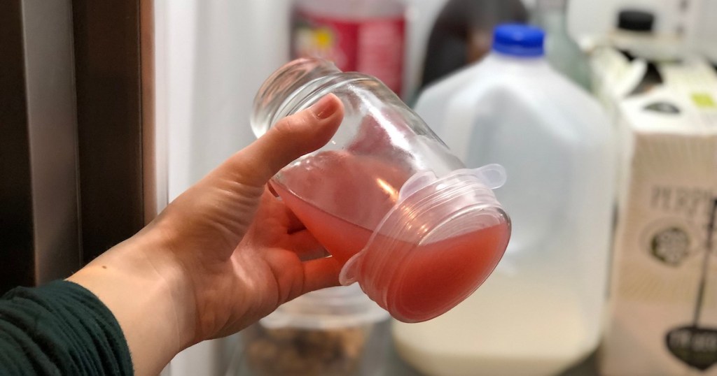hand holding glass cup with pink juice and silicone lid