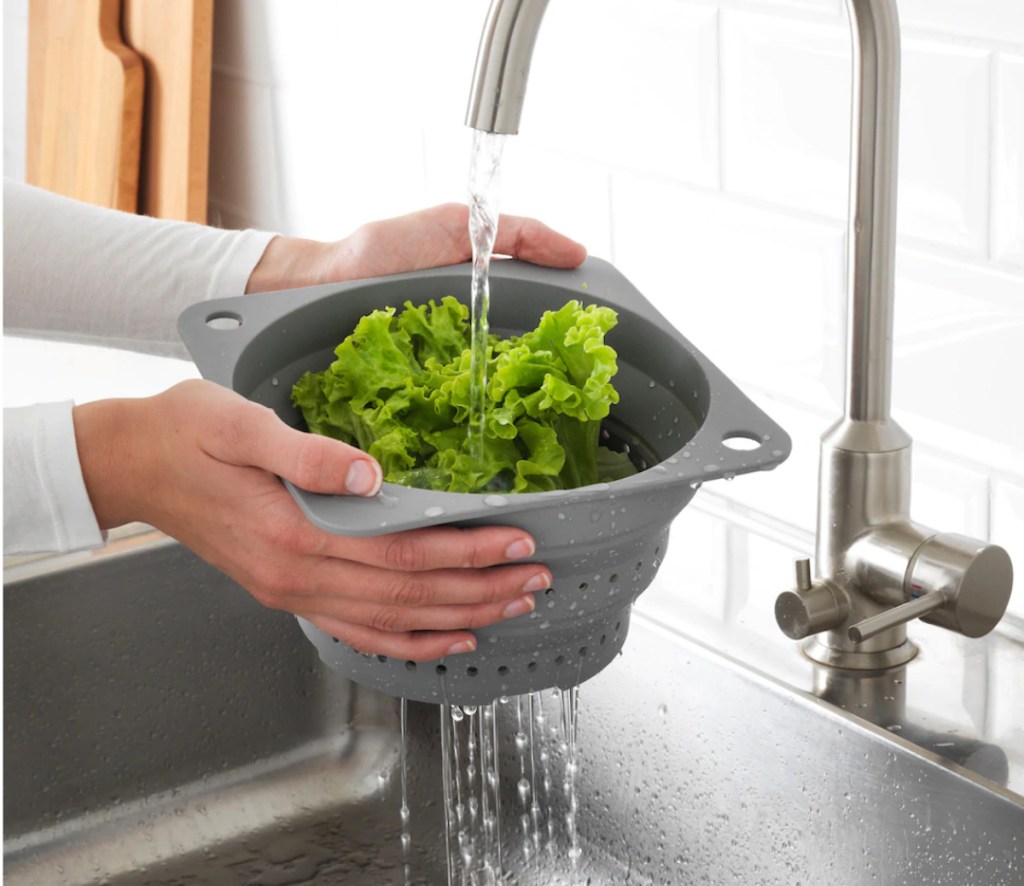 hands holding strainer over sink with wet green lettuce salad