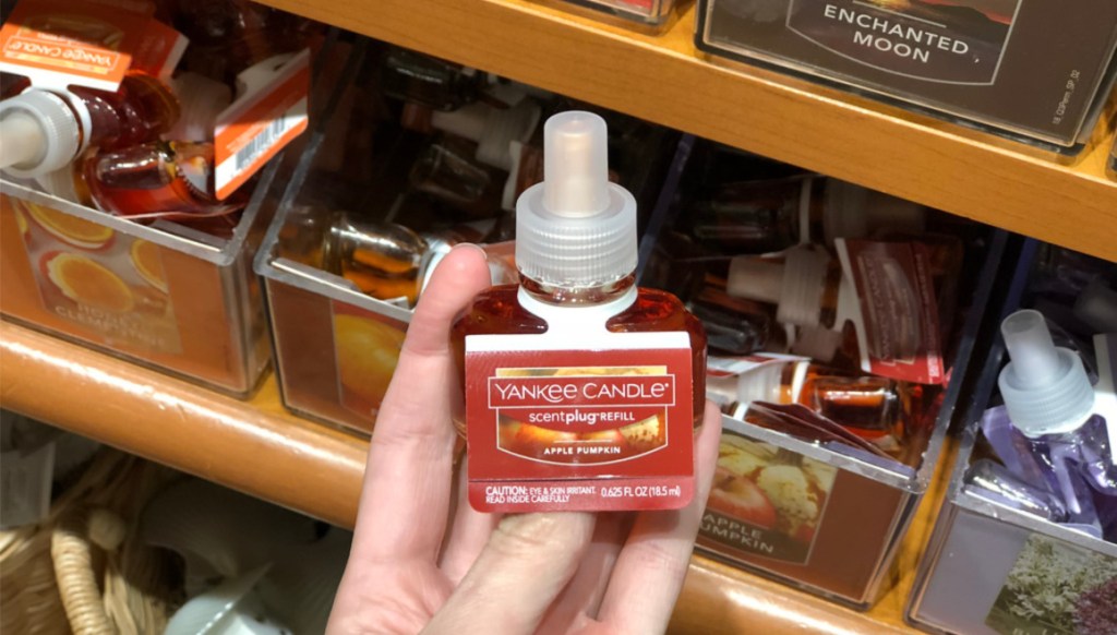 hand holding yankee candle apple pumpkin scentplug in store with other scentplugs in background