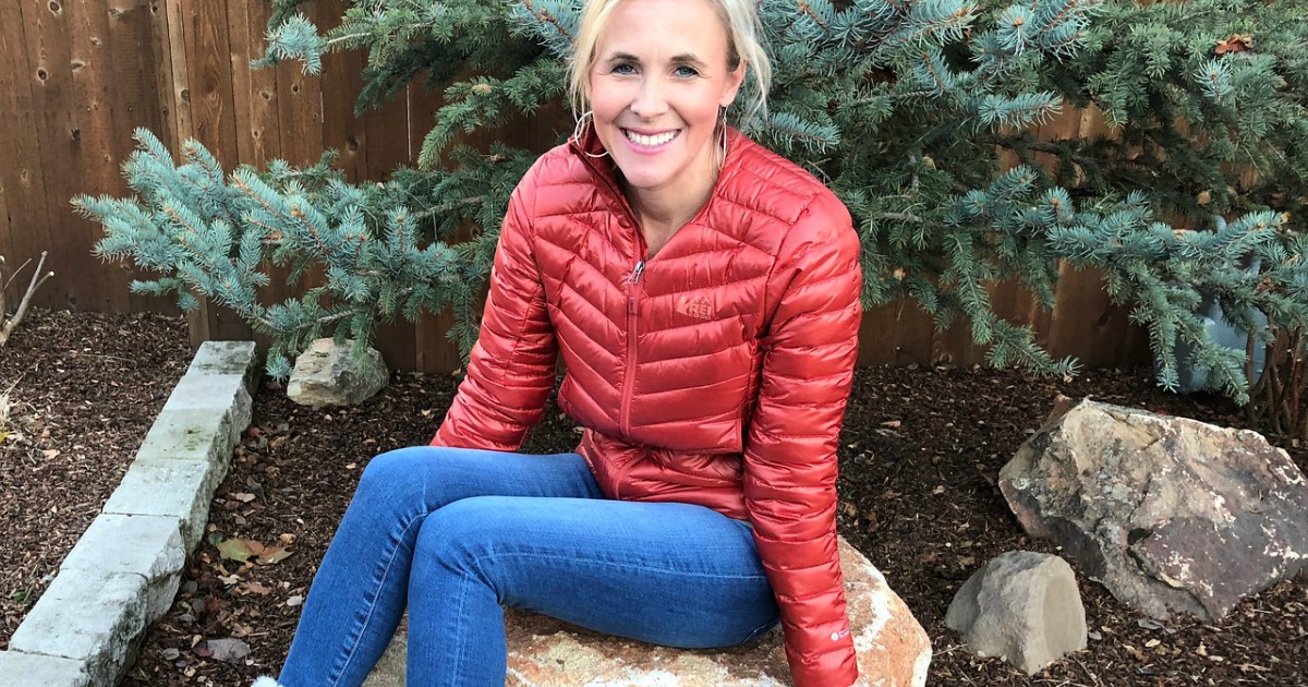 Woman wearing an REI Co-op Jacket and jeans while sitting on a rock