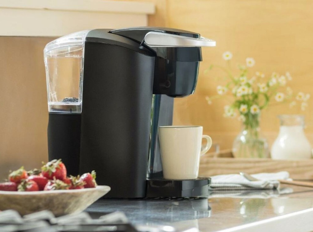 keurig sitting on kitchen counter with mug and bowl of strawberries