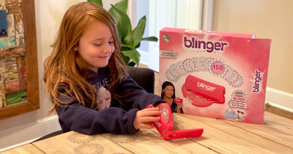 girl sitting at wood table with blinger deluxe box and toy