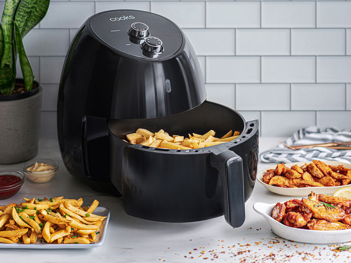cooks air fryer with basket out displaying fries and fried foods in background