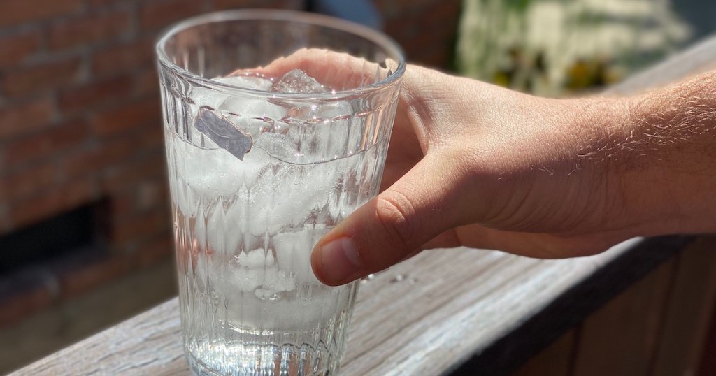 hand holding clear glass of ice water