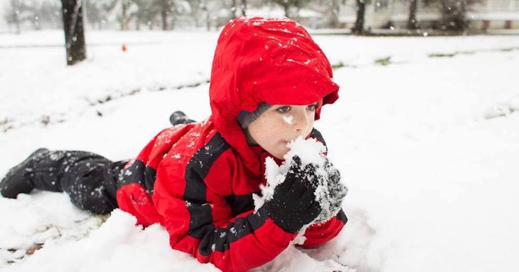 kid laying in snow wearing red jacket