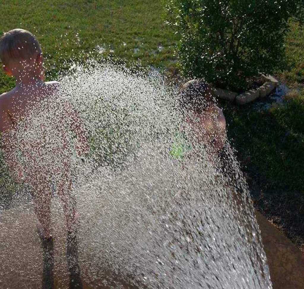 toddlers standing outside barefoot and naked with hose