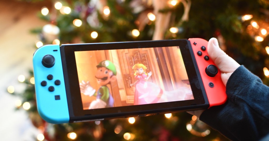 hand holding a nintendo switch toy in front of christmas tree