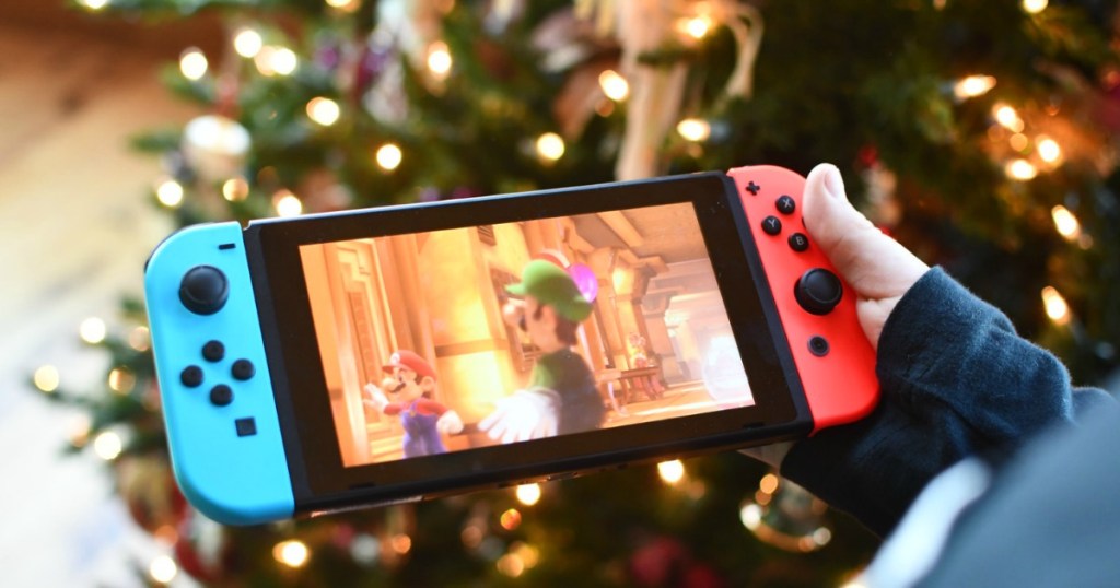 holding Nintendo Switch by Christmas tree