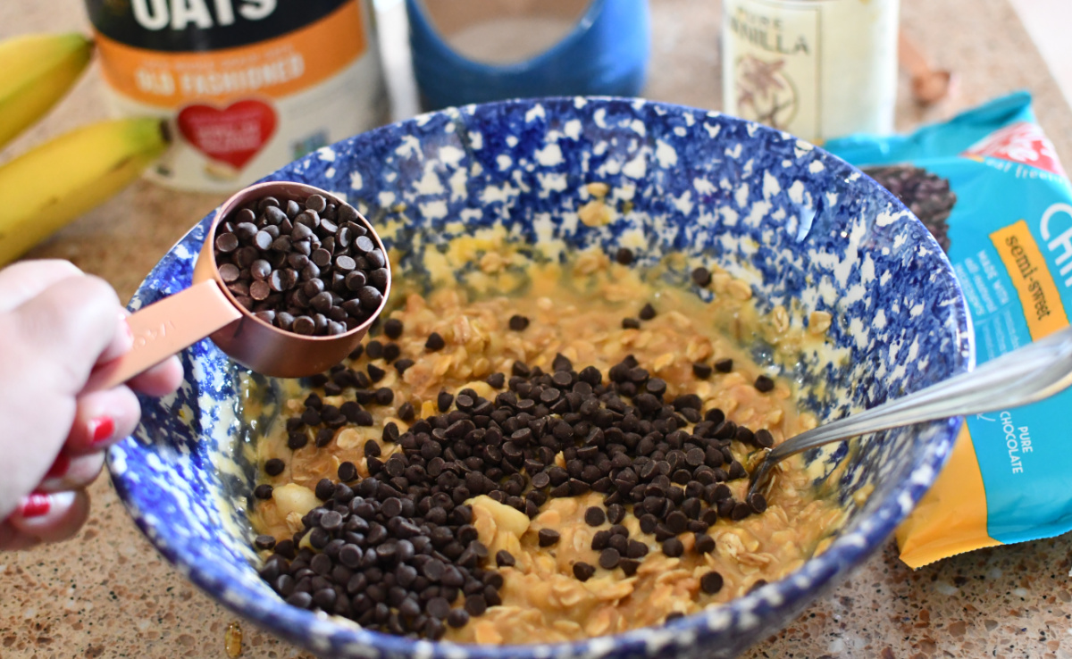 Adding chocolate chips to a mixing bowl in order to make peanut butter oatmeal chocolate chip bars