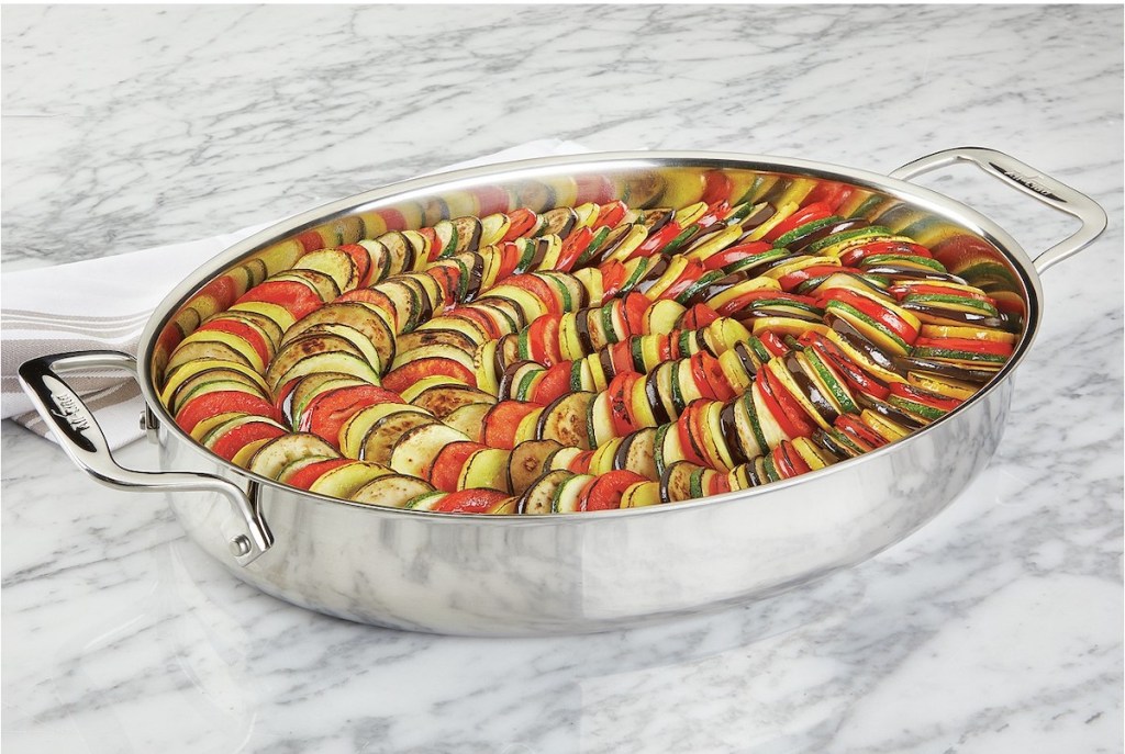 All-Clad Stainless Steel 15 Oval Baker with Pot Holders on marble background with tomatoes, zucchini, and squash sliced