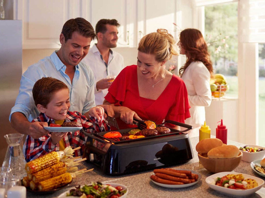 Family standing around indoor smokeless grill cooking