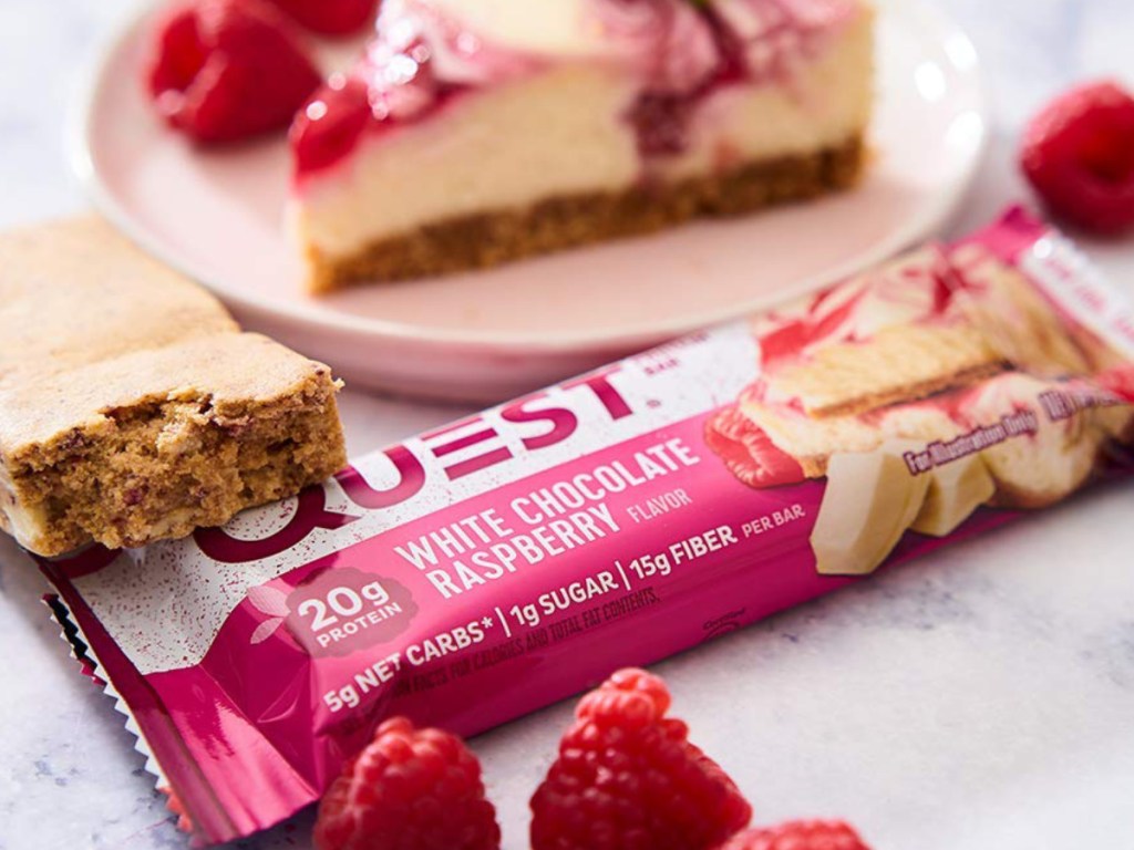 White Chocolate Raspberry Quest Nutrition Bar sitting with cheesecake and raspberries