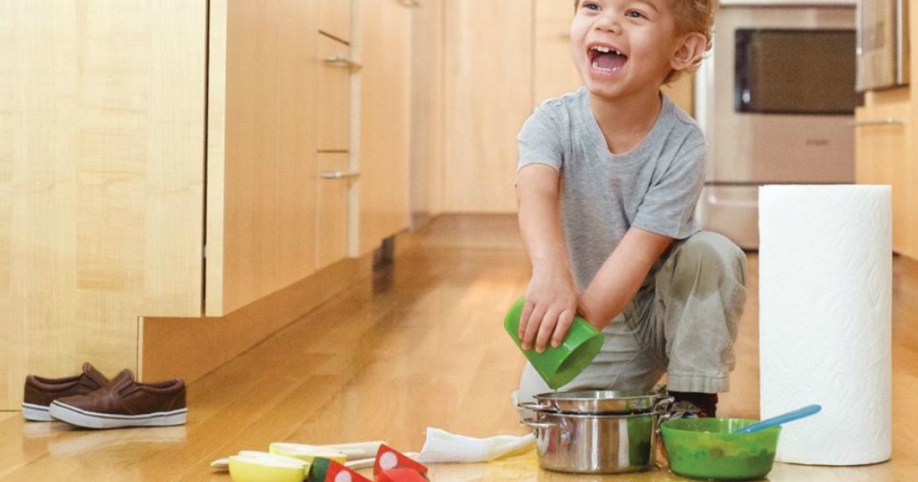 toddler boy playing on the kitchen floor next to a roll of paper towels