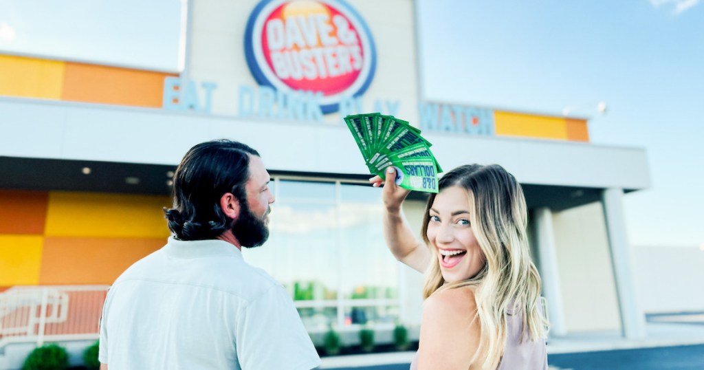 couple standing in front of dave and busters storefront holding d&b dollars