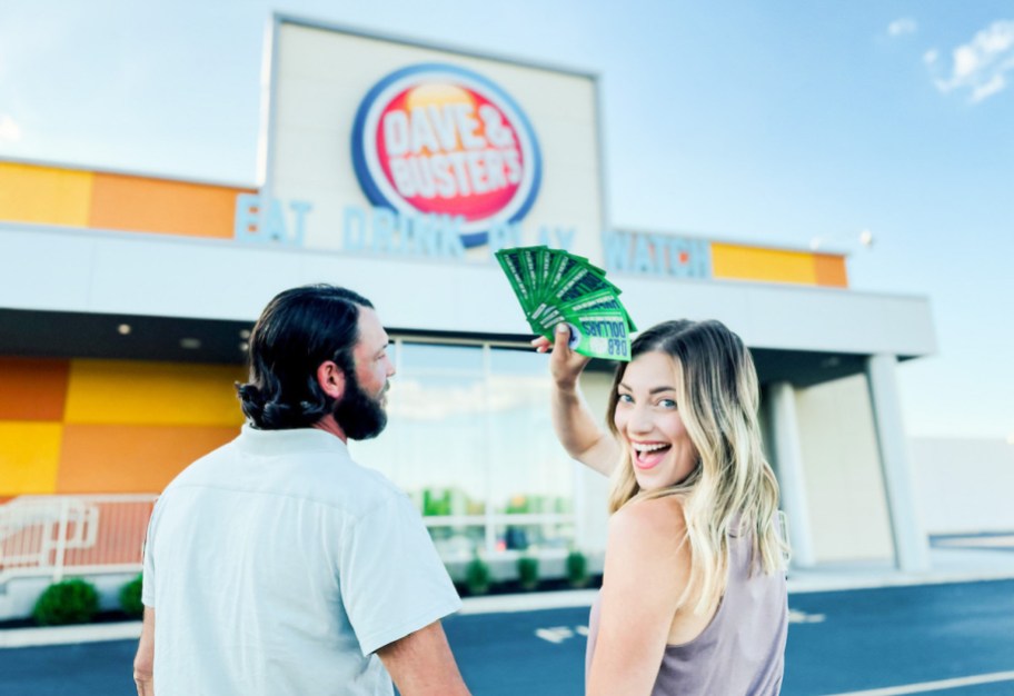 couple standing in front of dave and busters storefront holding d&b dollars