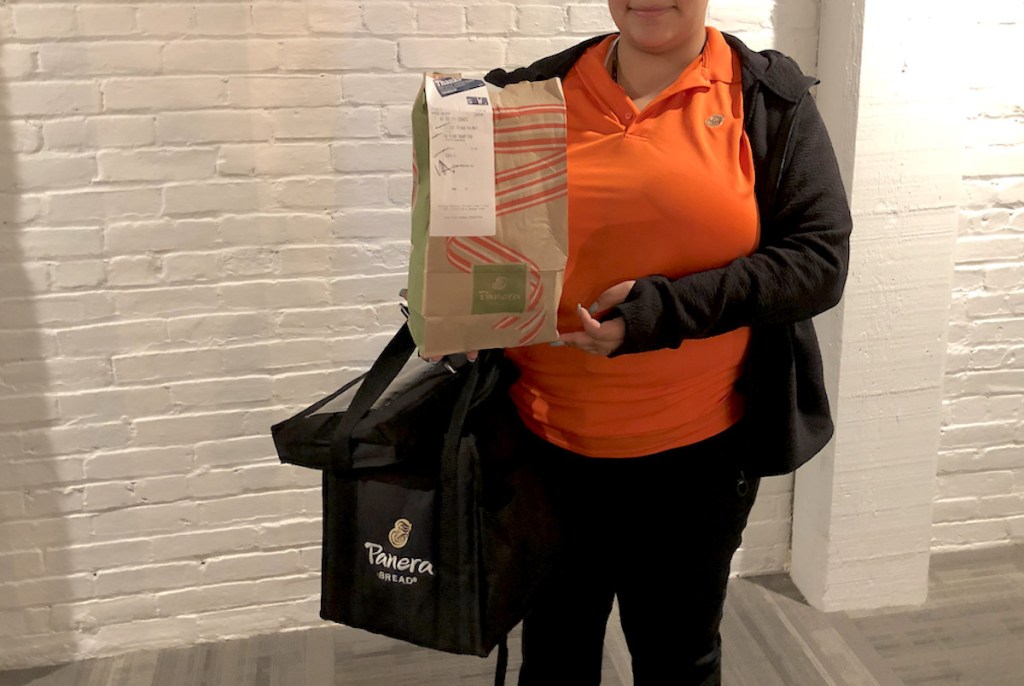 woman wearing orange shirt holding a panera bag and carry tote