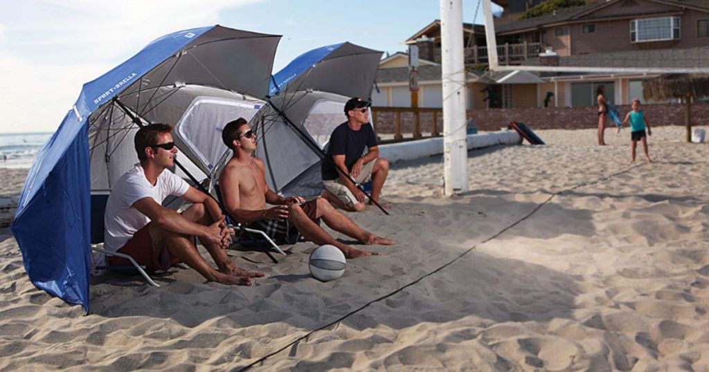 adults sitting in the sand under eight foot sport-brella