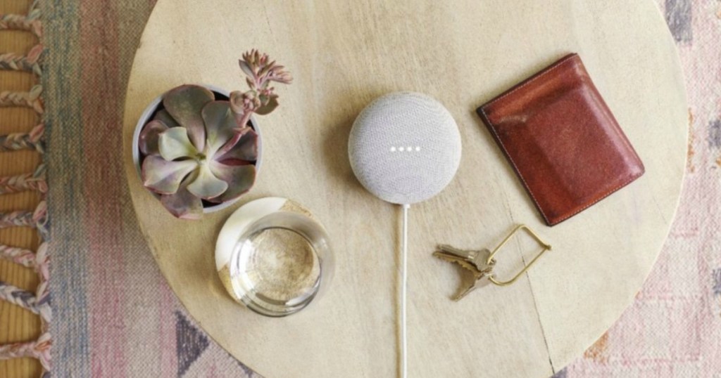 Google Nest Mini on table next to a glass of water, cactus, wallet and keys
