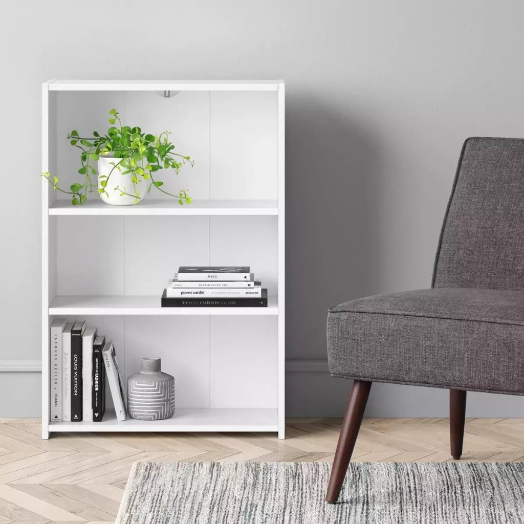 white Room Essentials 3 Shelf Bookcase in room next to grey fabric chair