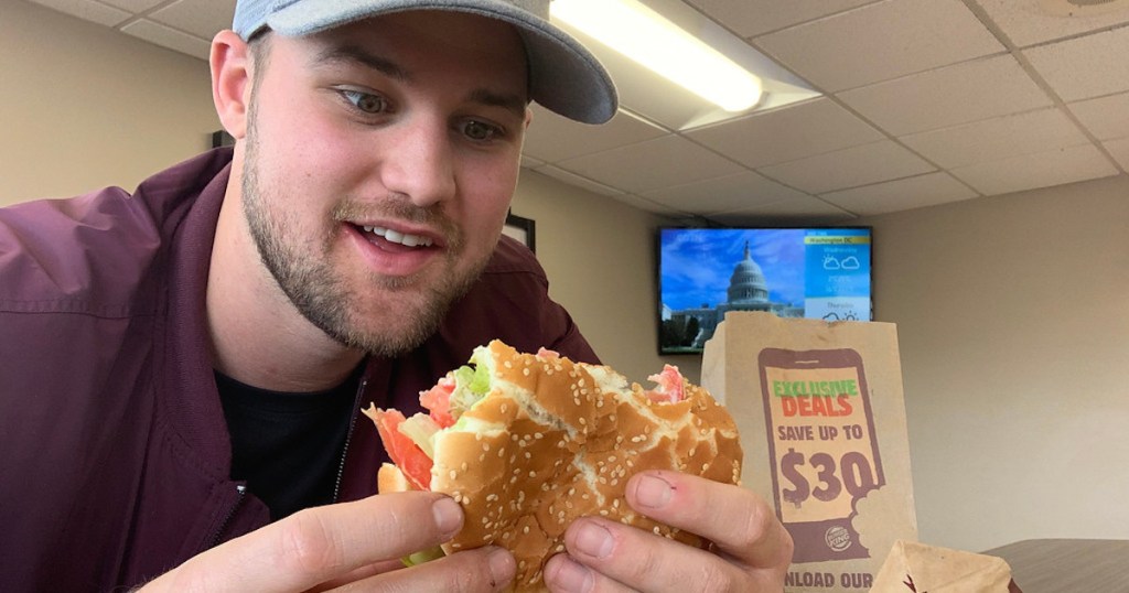 man sitting in fast food restaurant smiling at burger