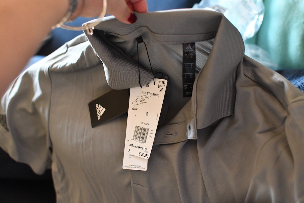 holding grey adidas polo shirt with price tag