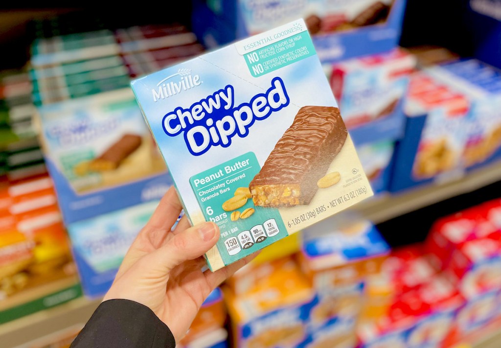 hand holding box of chewy dipped peanut butter bars in front of store shelves