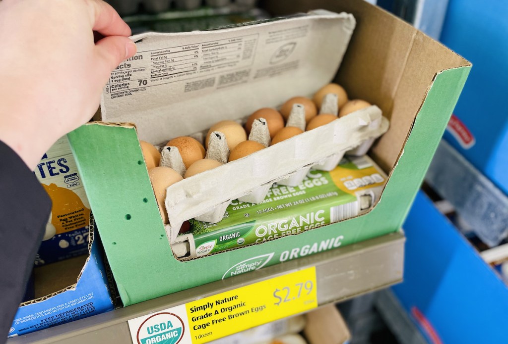 hand holding carton of brown eggs open in store fridge