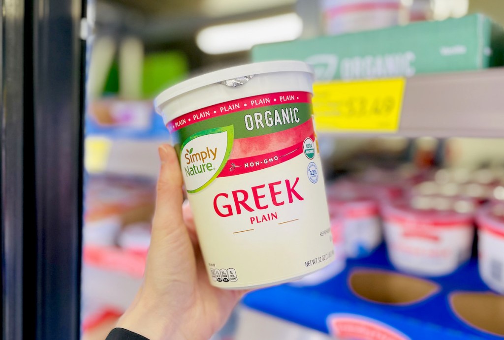 hand holding container of organic green plain yogurt in front of refrigerator