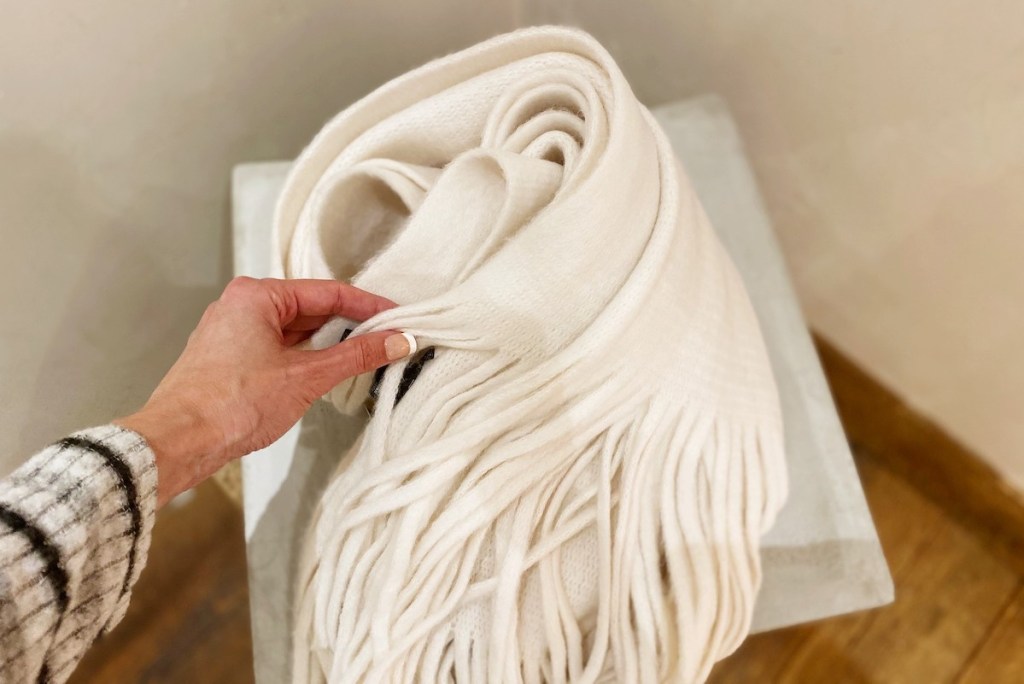 hand touching white fringed scarf