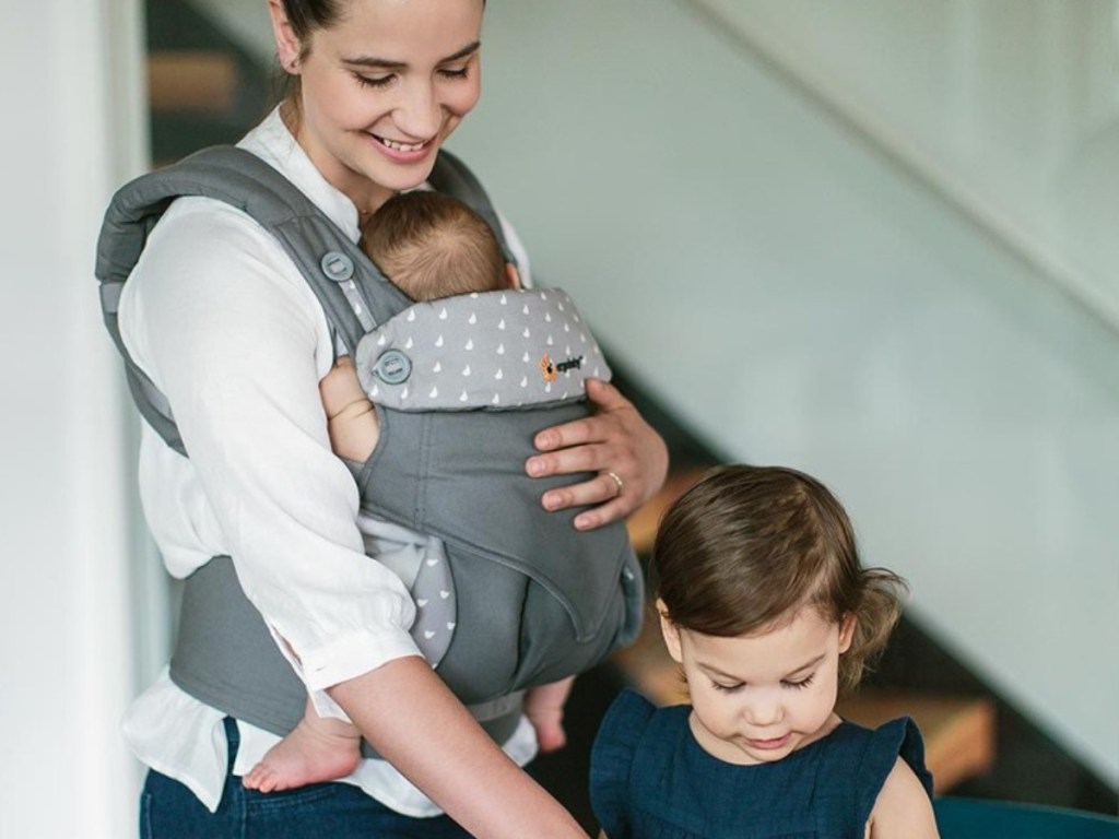 woman holding baby in baby carrier while helping other daughter