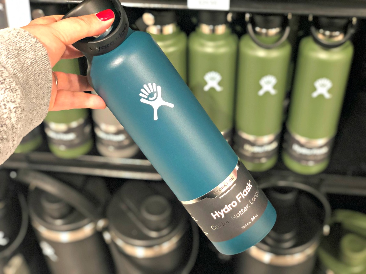 hand holding hydro flask blue water bottle with green on shelf in background