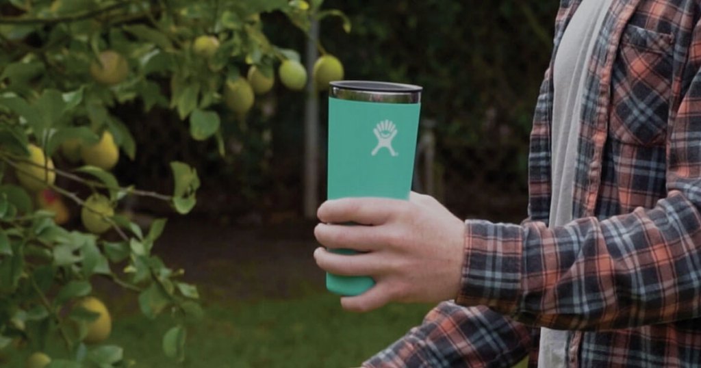 man holding a 32 oz hydro flask tumbler in mint next to trees