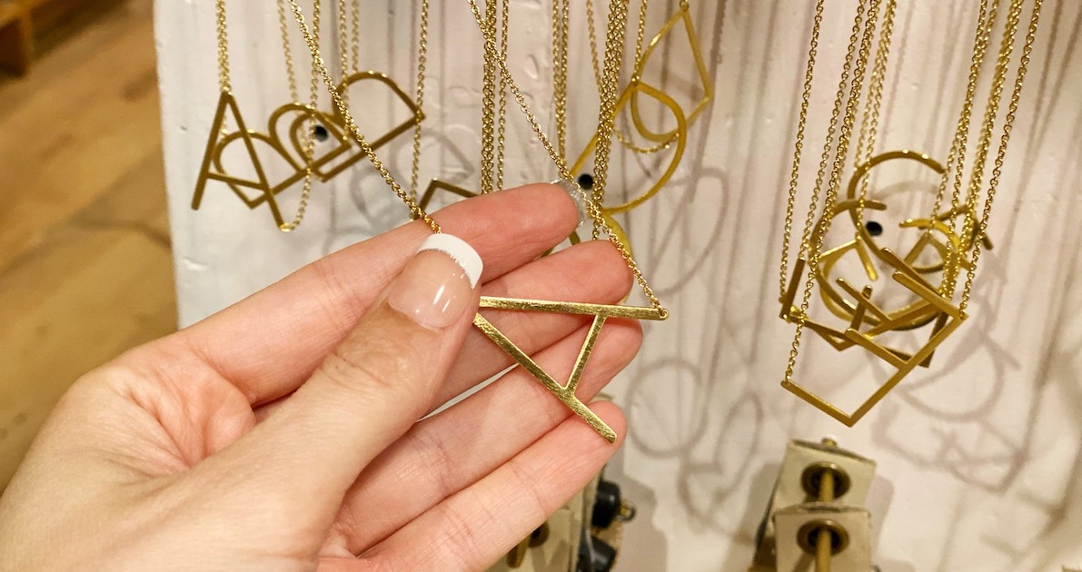 hand holding a gold A necklace with others hanging on store shelf
