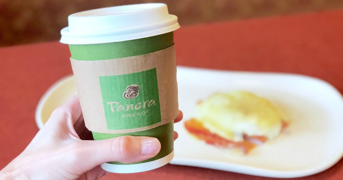 hand holding a panera coffee cup in front of a tray with a breakfast sandwich