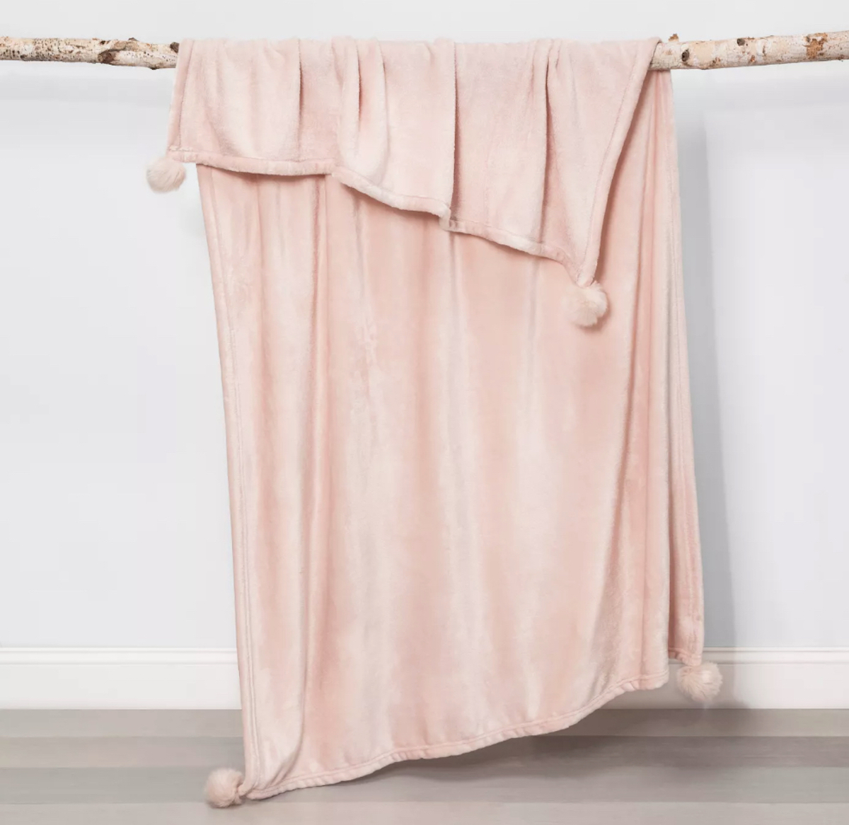 light pink soft throw blanket hanging from wood branch 