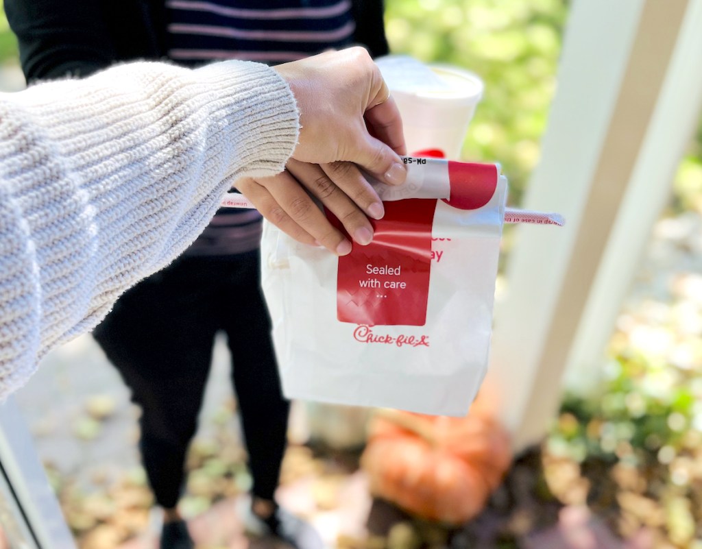 hand holding chick fil a takeout bag on front porch