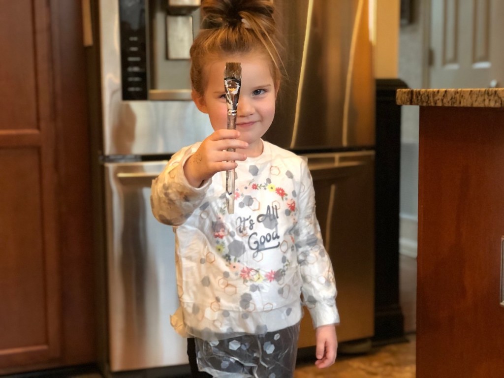 little girl wearing press n seal on her clothes holding a paint brush 