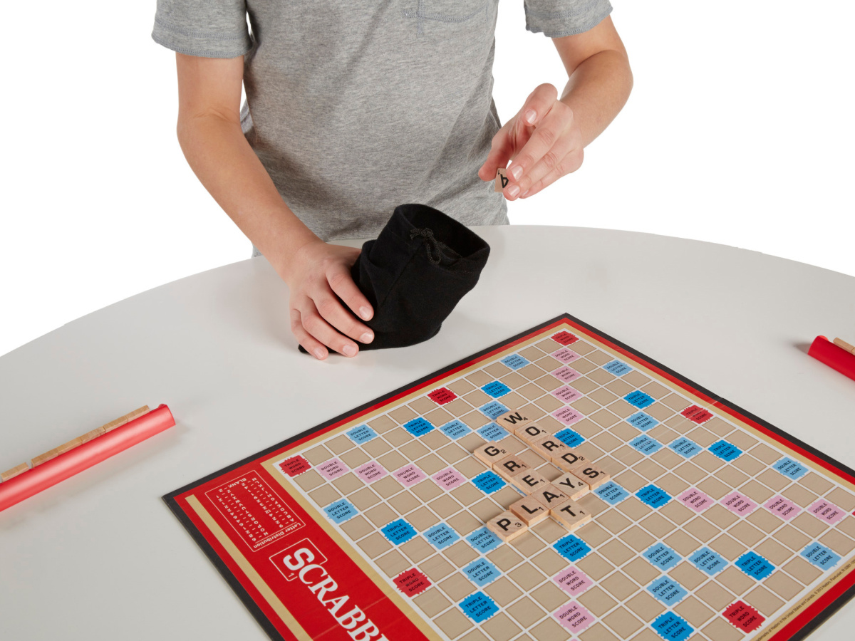 A person drawing Scrabble tiles out of the bag while the game sits on the table