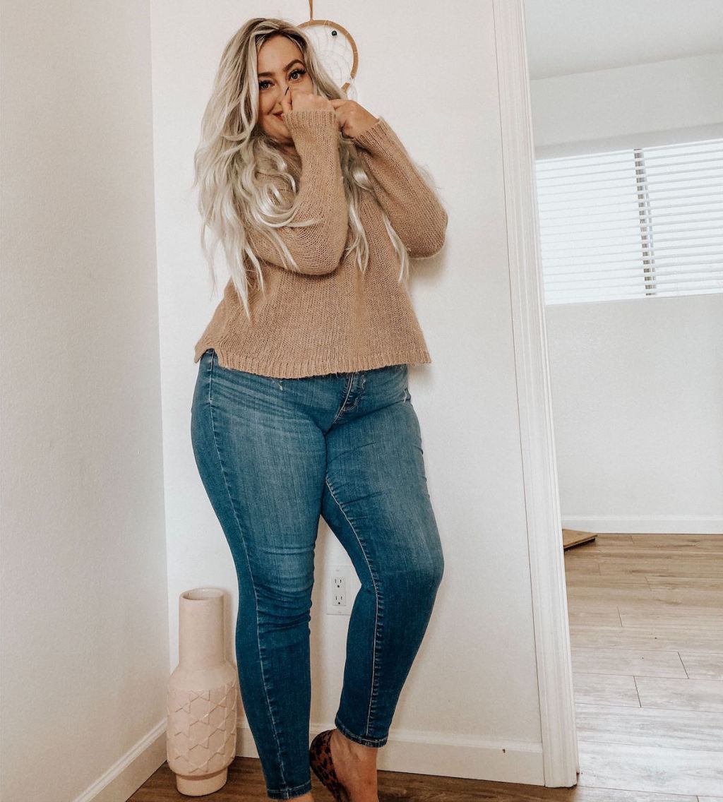 woman standing in corner of room wearing jeans and brown sweater