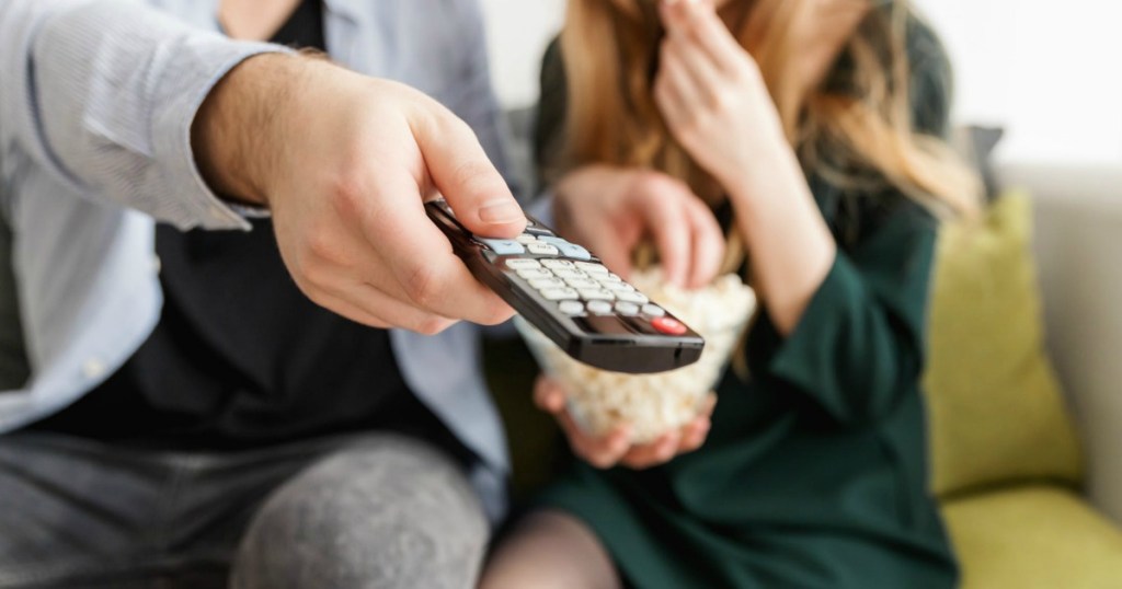 man holding remote control by woman eating popcorn