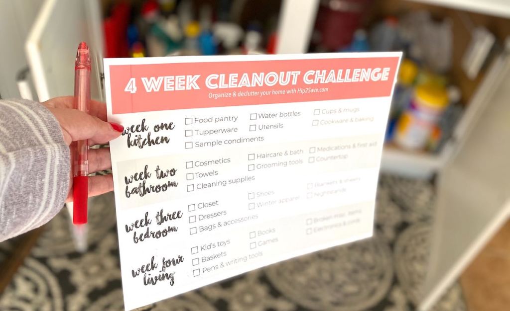 hand holding paper with 4 week declutter your home cleanout challenge checklist