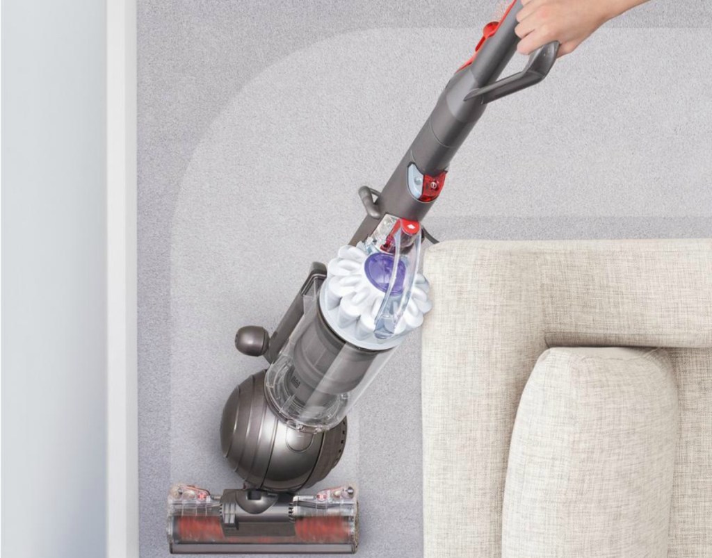woman pushing vacuum cleaner around a couch corner