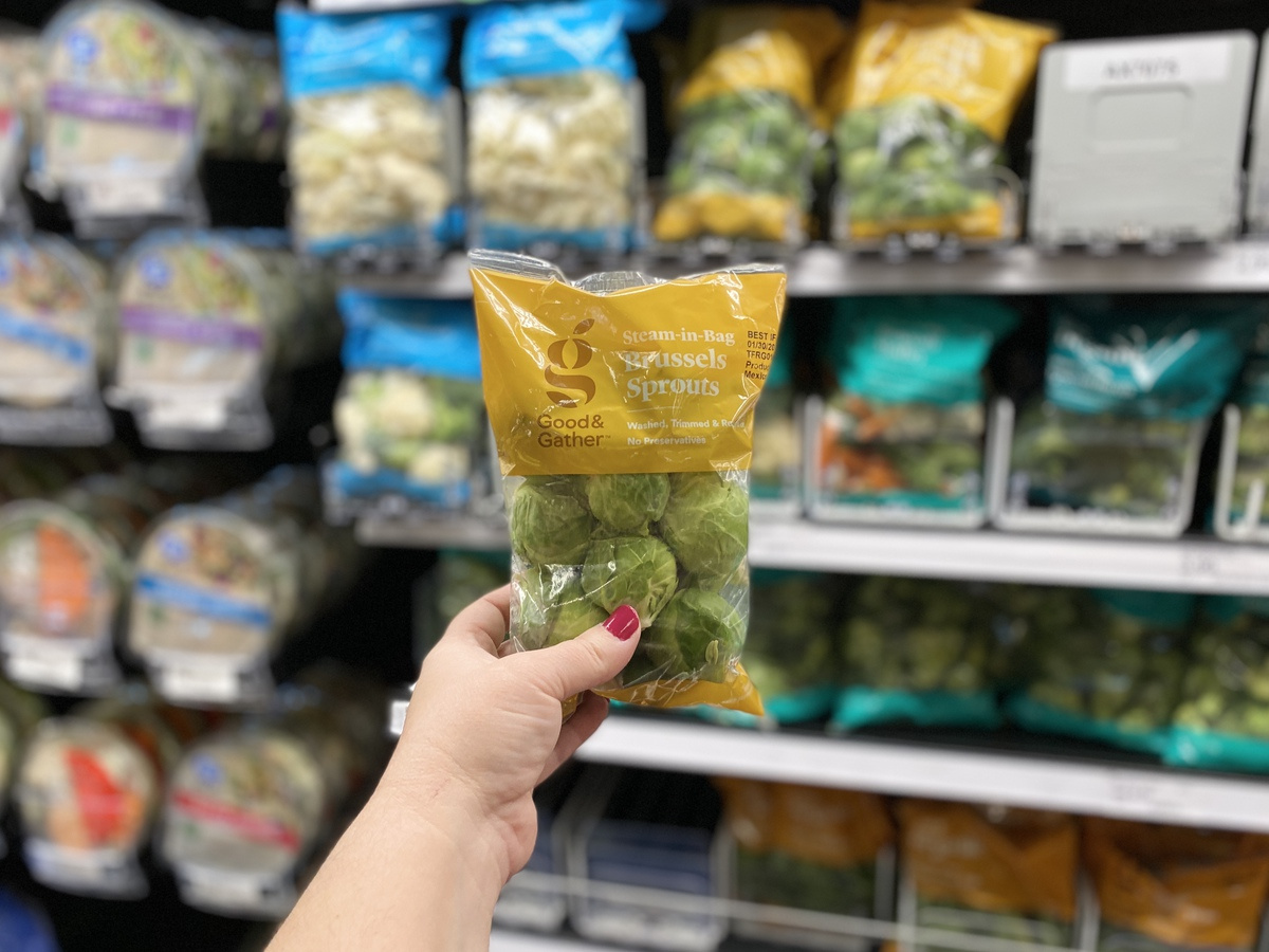 hand holding Brussels sprouts bag in store with produce in background