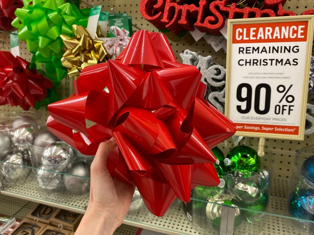 woman holding a large red holiday bow in front of in-store clearance display!