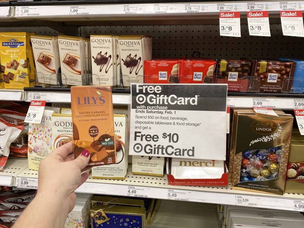 Woman's hand holding Lily's Chocolate Bar next to Target grocery sale sign
