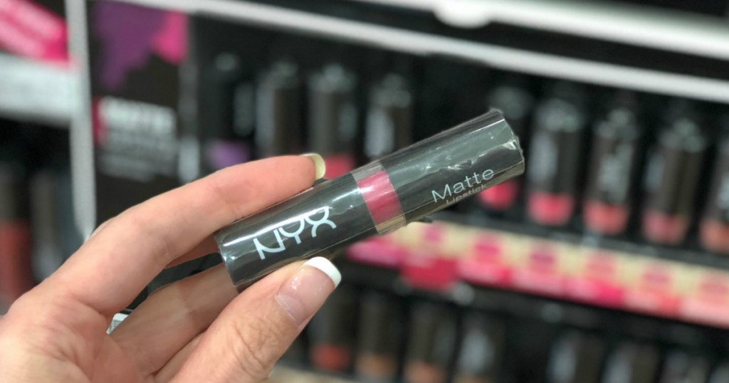 hand holding a tube of lipstick in a pink shade near in-store display
