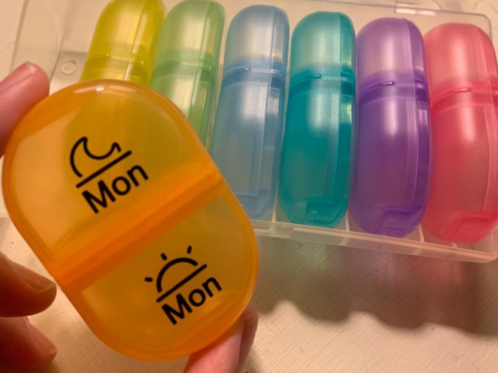hand holding yellow Auvon Pill container with pill organizer in background 
