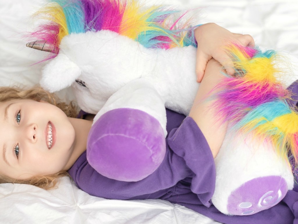 Young girl holding a plush unicorn with rainbow hair
