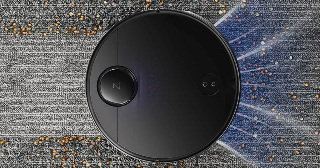 black robot vacuum passing over trail of crumbs on a gray carpet