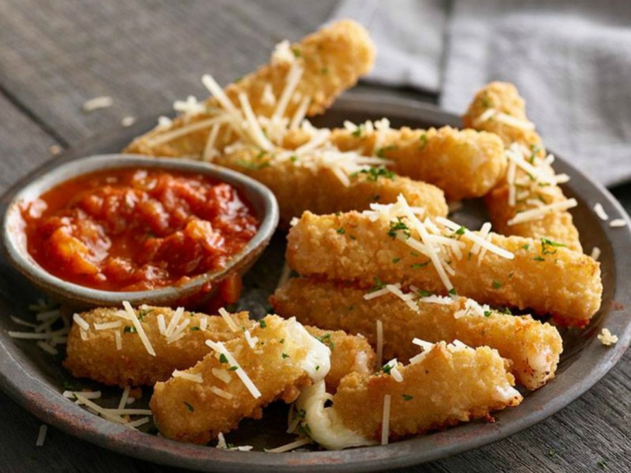 Large plate full of fried mozzarella sticks with a dipping container of marinara sauce